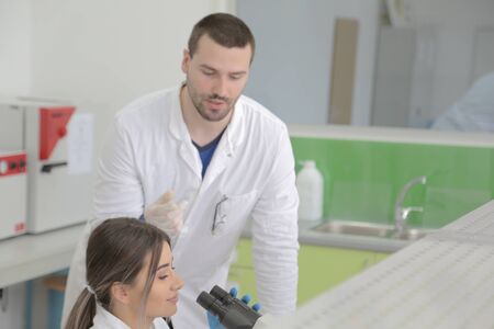 Two Young Female and male Laboratory scientists working at lab with test tubes and microscope, test...