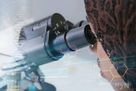 Young african muslim female scientist looking through a microscope in a laboratory doing research,...