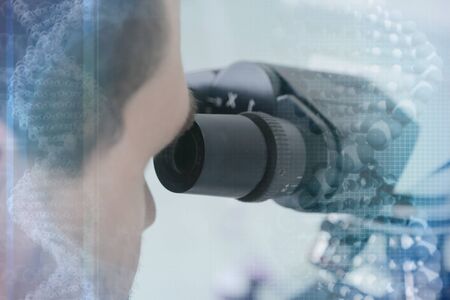 Young male male scientist looking through a microscope in a laboratory doing research,...
