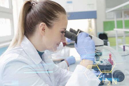 Young female scientist looking through a microscope in a laboratory doing research, microbiological...