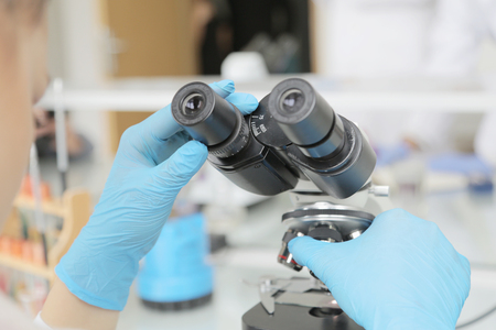 Young female male scientist looking through a microscope in a laboratory doing research,...