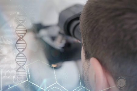Young male male scientist looking through a microscope in a laboratory doing research,...