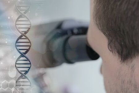 Young male male scientist looking through a microscope in a laboratory doing research,...