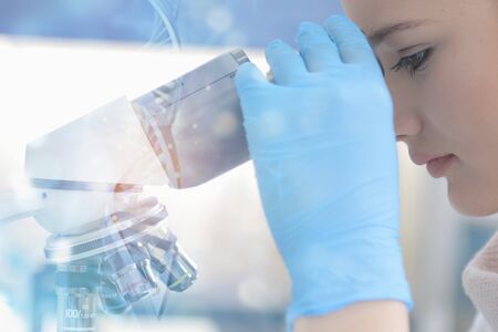 Young female male scientist looking through a microscope in a laboratory doing research