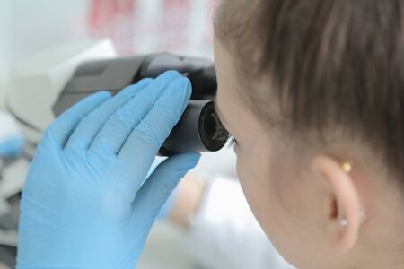 Young female male scientist looking through a microscope in a laboratory doing research,...