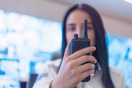 Security guard monitoring modern CCTV cameras in surveillance room. Female security guard in surveillance room. Female security guard holding portable radio in hand at workplace.の写真素材
