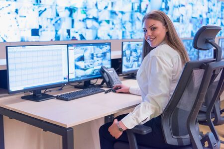 Security guard monitoring modern CCTV cameras in surveillance room. Female security guard in surveillance room. Smiling into camera.