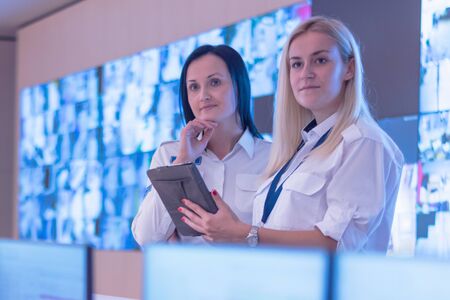 Two security guards working on computers while sitting in the main control room, CCTV surveillance.の写真素材