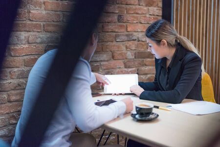 Two young male and female multiracial business people working connected with technological devices at the bar. Two young creative coworkers working with new startup project.の写真素材