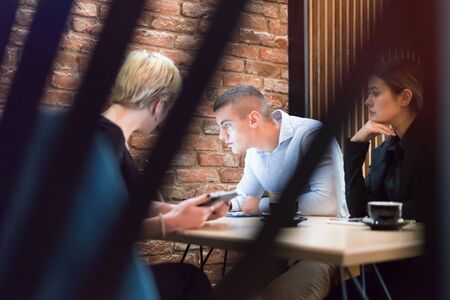 Multiracial business people working connected with technological devices at the bar. Group of three young creative coworkers working with new startup project.の写真素材