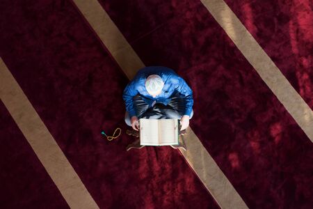 Young Arabic Muslim man reading Koran and praying. Religious muslim man reading holy koran inside...