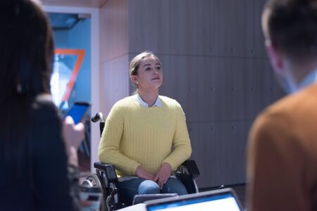 Handicapped young woman with colleagues working in office. She is smiling and passionate about the workflow. Performing in co-working space. Office people working together.の写真素材