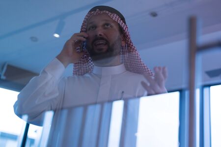 Middle Eastern businessman talking on the phone and looking out the window in his office....