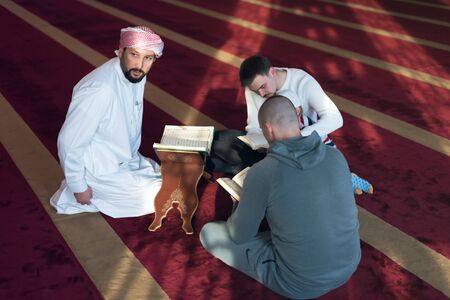 Group of muliethnic religious muslim young people praying and reading Koran together inside beautiful modern mosque.の写真素材