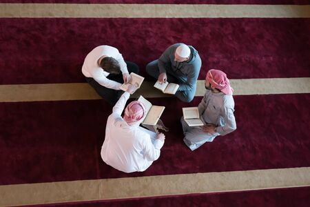 Group of muliethnic religious muslim young people praying and reading Koran together inside beautiful modern mosque.の写真素材