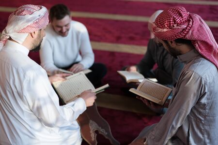 Group of muliethnic religious muslim young people praying and reading Koran together inside...