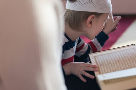 Religious Muslim Man teaching his little son to pray to God with Koran and rosary at mosque during ramadan.の写真素材