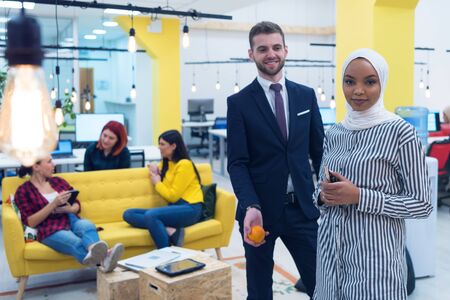 Portrait of young bearded Caucasian businessman dressed smart casual and african hijab woman posing inside modern coworking space.の写真素材