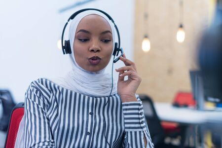 African muslim female with hijab scarf customer representative business woman with phone headset helping and supporting online with customer in modern bright call centre.の写真素材