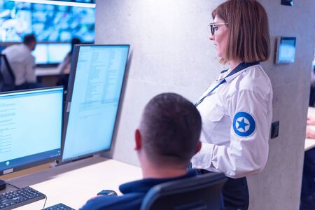 Two security guards working on computers while sitting in the main control room, CCTV surveillance.の写真素材