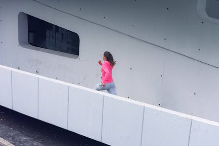 Young female woman running outdoors in urban road. Young female exercising in sport clothes.