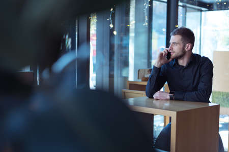 Portrait of young bearded Caucasian businessman dressed smart casual using phone inside modern coworking space.の写真素材