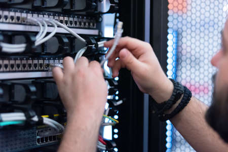 An Expert Engeneer in datacenter server room  connecting cables in server cabinet in network server room.の写真素材