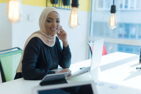 Muslim business lady wearing hijab and working at computer in office. Pretty african woman in hijab...