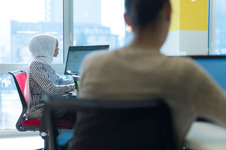 Pretty african muslim business womanand her female american colleague at work sharing office desk...