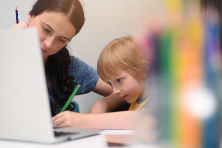 Coronavirus Outbreak. Lockdown and school closures. Mother helping her son studying online classes...