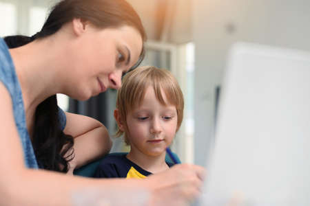 Coronavirus Outbreak. Lockdown and school closures. Mother helping her son studying online classes at home. COVID-19 pandemic forces children and teachers online learning.の写真素材