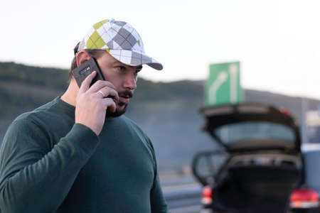 Man calling road assistance on the highway. Calling car service, assistance or  tow truck while having troubles with his car.の写真素材