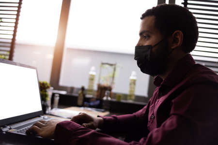 African businessman or developer wearing surgical face mask in the restaurant and typing on laptop - concept on new normal everyday lifestyle and people at work in covid-19 pandemic season.の写真素材