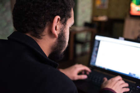 Young black male  developer sitting in pizza restaurant, drinking coffee or  tea and working with laptop.の写真素材