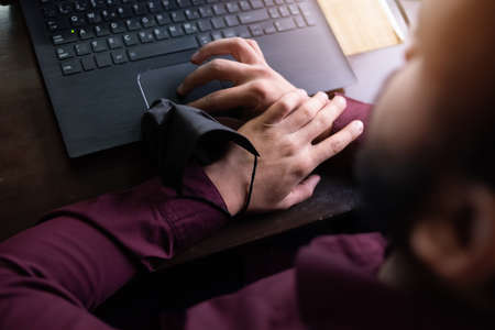 African businessman or developer wearing surgical face mask in the restaurant and typing on laptop -...