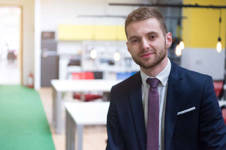 Portrait of young bearded Caucasian businessman dressed smart casual posing inside modern coworking space.