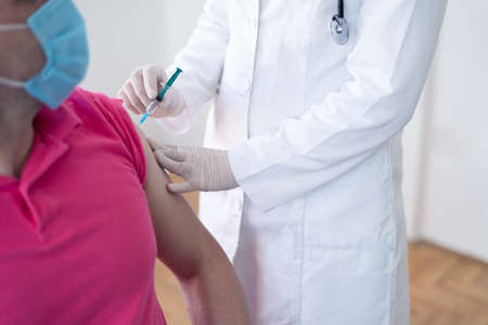 Young Female doctor in protective mask injecting or preparing for injecting vaccine into patient's armの写真素材