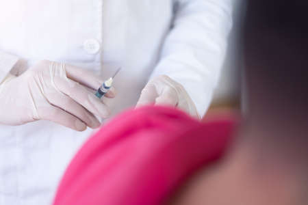 Young Female doctor in protective mask injecting or preparing for injecting vaccine into patient's...