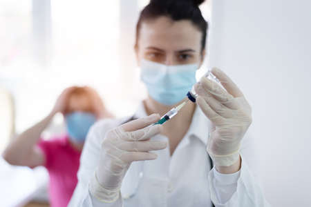 Young Female doctor in protective mask injecting or preparing for injecting vaccine into patient's armの写真素材