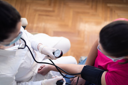 Female doctor using sphygmomanometer with stethoscope checking blood pressure to a patient in the...