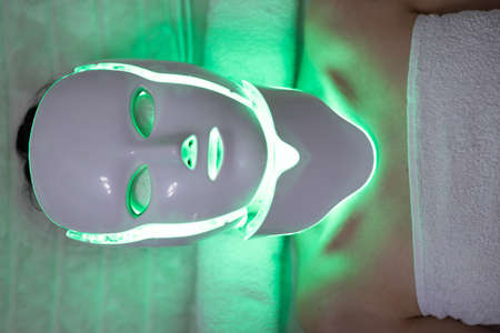 LED mask regenerative treatment applied to a young woman. Woman with led light therapy facial and neck beauty mask photon therapyの写真素材