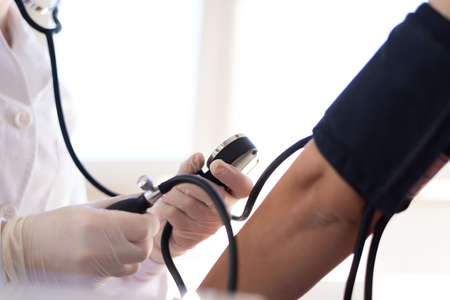 Female doctor using sphygmomanometer with stethoscope checking blood pressure to a patient in the hospitalの写真素材