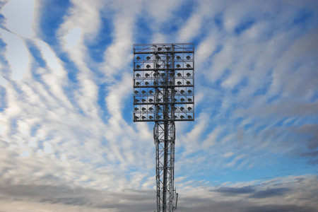 Spotlights on a lighting mast over the stadium against the blue sky with white clouds on a dayの写真素材