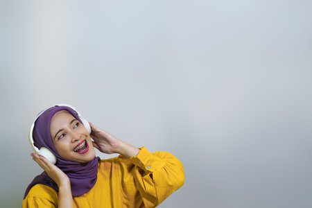 Happy muslim girl in wireless headphones listening music online on smartphone, enjoying new app white backgroundの写真素材