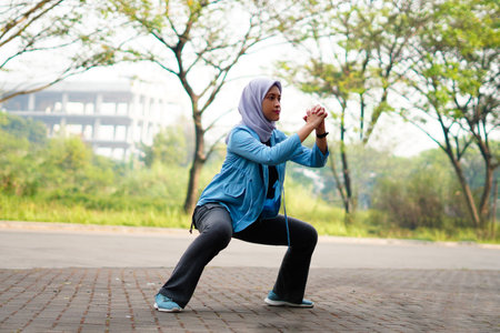 Beautiful Muslim woman working out outdoors in the morning. Sporty woman with a hijab warming up by doing exercises.の写真素材