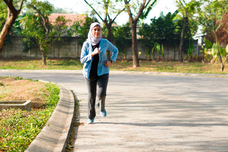 Happy slim Hijab woman wearing sportswear jogging in at sunrise. Young beautiful asian female...