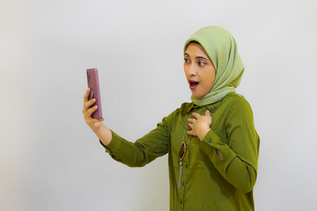 Happy Young Asian woman holding her phone for advertising concept. Green outfit hijab woman concept