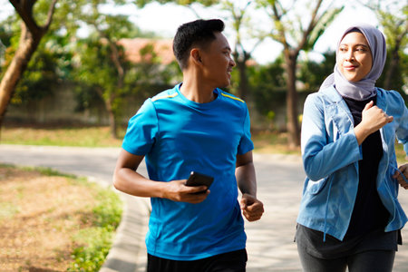 Young muslim couple happy together running at green summer park. Man and woman in hijab doing morning workout outdoors.の写真素材
