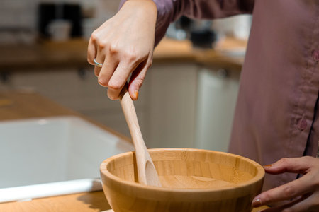 a woman's hand holding a wooden spatula making dough with a wooden bowl, close-up shot in the...