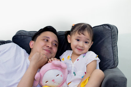 Father and daughter bonding, playing together, lying on sofa in family room.
